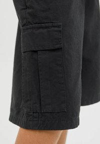 Shorts cargo noirs avec une poche latérale, un tissu texturé et un ourlet droit. Le design est fonctionnel avec des accents utilitaires.