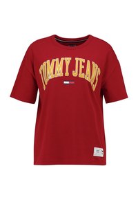 Camiseta de algodón roja con un corte relajado, que presenta un logo amarillo de "TOMMY JEANS" y un pequeño detalle de bandera tricolor cerca del escote.