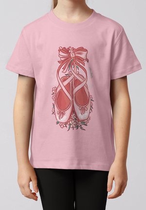 Kind trägt ein rosa T-Shirt mit einer Grafik von rosa Ballettschuhen, die mit Bändern gebunden sind und von kleinen Blumen umgeben sind.