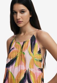 Top a coppe multicolore con pieghe, caratterizzato da grandi motivi floreali in rosa, arancione, verde e nero. Tessuto leggero, spalline sottili.