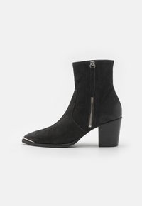 Cizmă neagră din microfibră cu vârf ascuțit, toc gros și fermoar lateral cu o apucare de ton argintiu. Textură netedă și design elegant.