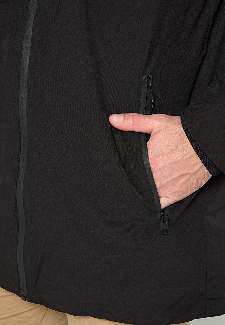 Zwarte jas met een ritssluiting aan de voorkant, textuurstof en zijzakken. Details van de ritssluiting zijn zichtbaar; de mouwen hebben elastische manchetten.