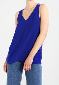 Kungsblå ärmlös topp med V-ringning, tillverkad av ett mjukt tyg. Har en lös passform och minimala sömmar för en ren look.