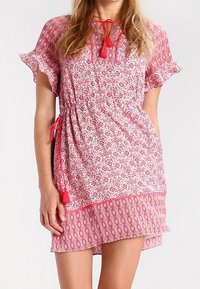 Krátké červenobílé šaty s květinovými a geometrickými vzory, volánkovými rukávy, stahovacími šňůrkami v pase a třásňovými akcenty. Poloprůhledná látka.