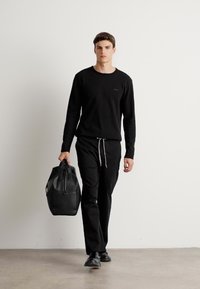 Sort langærmet t-shirt, sorte drawstring bukser og sorte sko. Modellen bærer en struktureret sort lædertaske. Minimalistisk design.