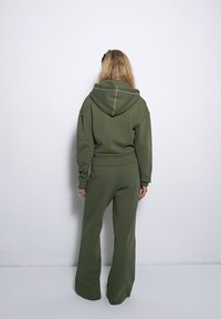 Zestaw odzieży do domu w kolorze oliwkowym, składający się z krótkiej bluzy z kapturem oraz spodni o szerokich nogawkach, wykonany z miękkiego materiału z minimalnymi detalami szwów.