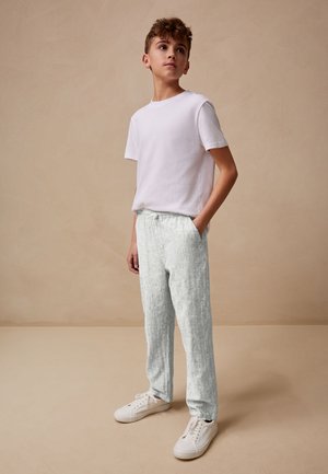 T-shirt en coton blanc et pantalon léger en lin texturé avec une taille élastique. Associés à des baskets blanches, le tout sur un fond neutre.