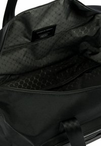 Intérieur de sac de voyage noir avec motif hexagonal, texture lisse, fermeture éclair et étiquette de marque. Design léger et spacieux.