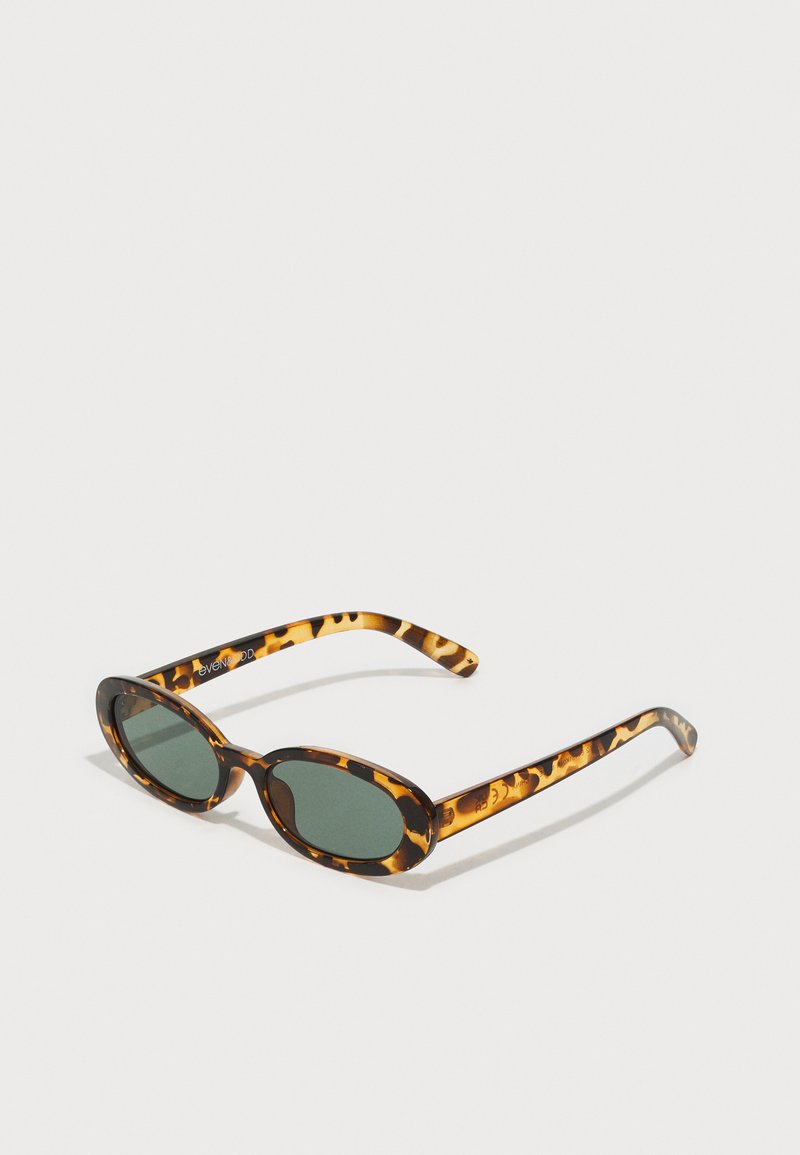 Tortoiseshell zonnebril met ovale monturen, donkergroene lenzen en slanke armen. Bevat een subtiele logo op de arm.