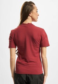 Kortærmet rød T-shirt med rund halsudskæring, tætsiddende design og glat tekstur, set fra ryggen med skulderlangt hår synligt.