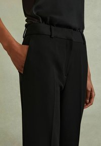 Fekete, szabott nadrág sima textúrával, oldalsó zsebekkel és slim fit szabással. A derékrészt övakasztók díszítik.