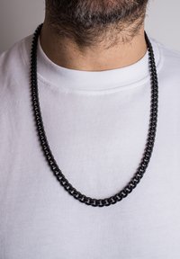 Sorte metal kædestens halskæde på en hvid t-shirt, med tykke led og en glat tekstur, samt en blank finish der reflekterer lyset.