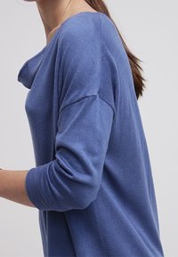 Pull bleu léger avec une coupe décontractée, un large col et des manches longues. Les poignets côtelés et la texture lisse augmentent le confort.