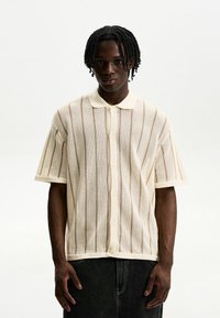 Cream-colored short-sleeve button-up shirt with a textured mesh pattern and vertical stripes, featuring a classic collar and relaxed fit.