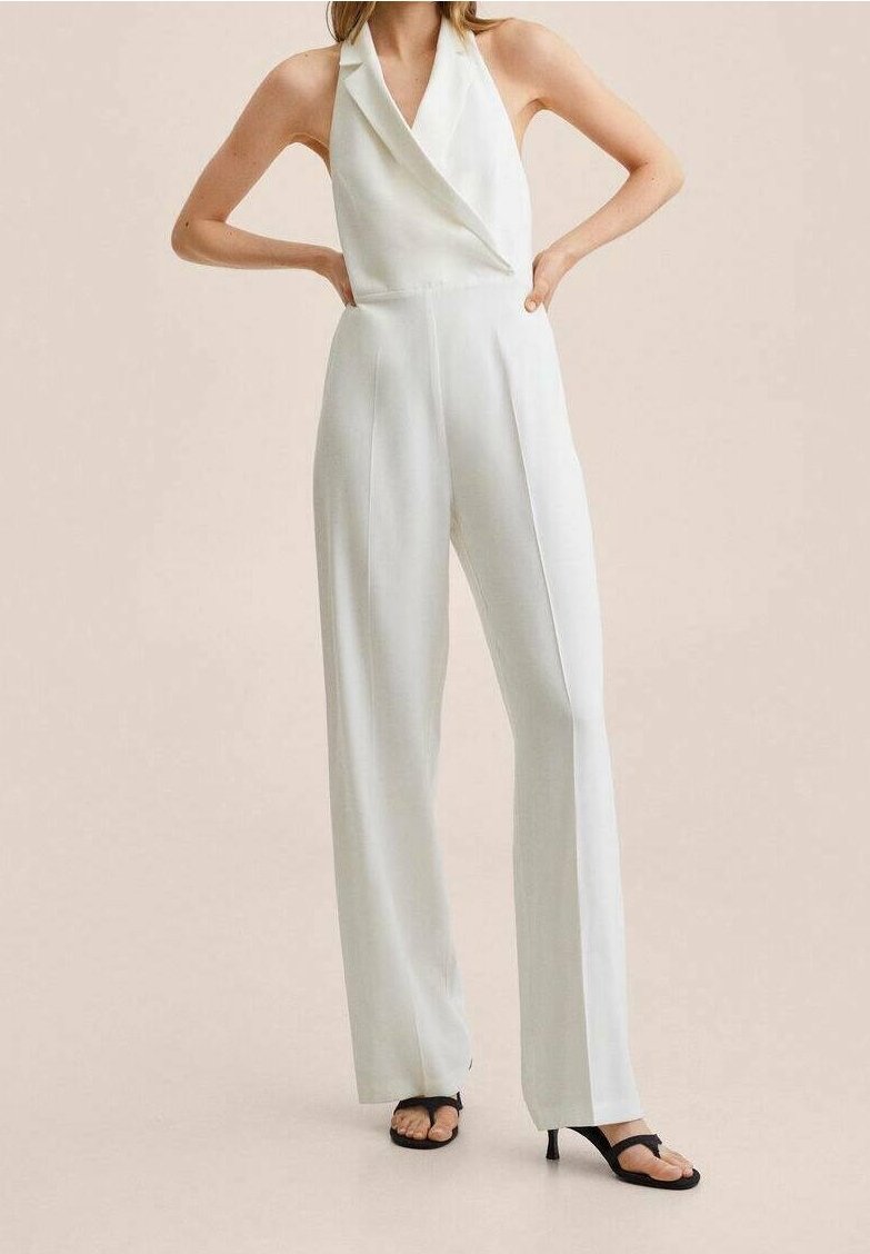 Combinaison blanche avec un décolleté halter, un design à jambes larges et un tissu lisse. Elle ne présente aucun motif visible et est complétée par des sandales noires.