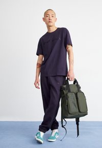 Marinblå T-shirt med svart logotyp, matchande marinblå joggers och teal sneakers. Oljefärgad ryggsäck med framfickor och justerbara axelremmar.