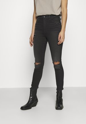 Jeans de mezclilla negros de cintura alta con detalles de rodilla rasgada, diseño ajustado y tejido texturizado, combinados con botines negros.
