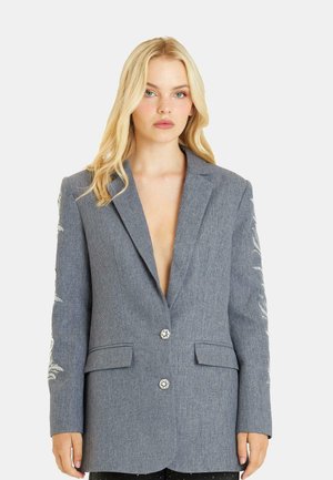 Blazer grigio con un design strutturato, scollatura a V profonda, ricami decorativi sulle maniche e due tasche frontali. Presenta una chiusura con due bottoni.
