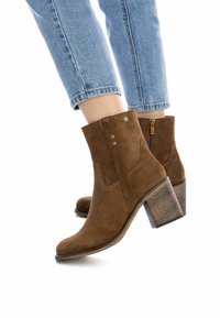 Stivaletti alla caviglia in suede marrone con punta appuntita, tacco medio a blocco e zip laterale. Presentano cuciture decorative e dettagli in tono oro.