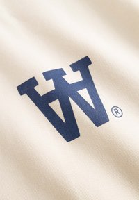 Le tissu crème présente un grand logo graphique bleu foncé avec un symbole de marque déposée, mettant en valeur une surface lisse et texturée.