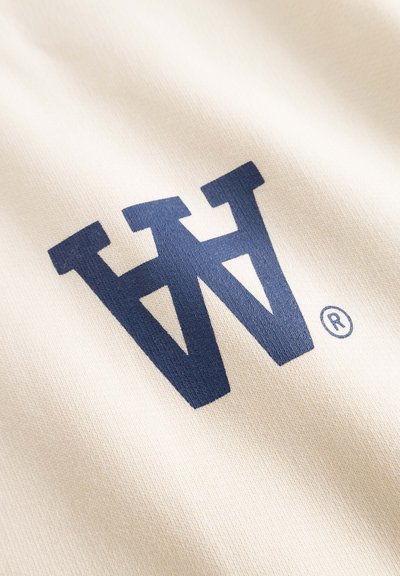 Le tissu crème présente un grand logo graphique bleu foncé avec un symbole de marque déposée, mettant en valeur une surface lisse et texturée.