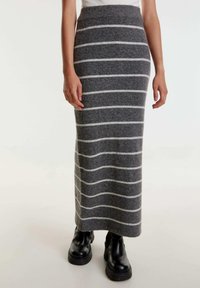 Grijze gebreide maxi rok met witte horizontale strepen. Zachte textuur, aansluitende taille en een rechte snit, gecombineerd met zwarte stevige laarzen.