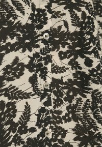 Blusa de botão em preto e branco com estampa de folhas de samambaia, com textura de tecido suave e botões redondos e transparentes na frente.