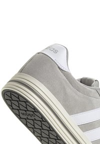 Baskets en daim gris avec des accents en cuir blanc, présentant trois rayures horizontales et une semelle en caoutchouc texturé pour une meilleure adhérence.