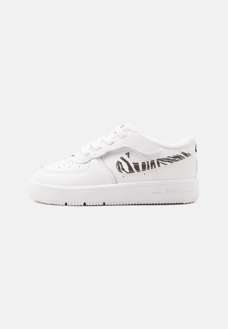 Λευκό αθλητικό παπούτσι Nike με μαύρο λογότυπο Swoosh με ρίγες ζέβρας στο πλάι, λευκά κορδόνια και υφασμένη σόλα σε μονόχρωμο φόντο.