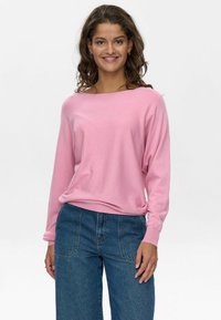 Suéter de manga larga de color rosa claro, con un escote ancho, corte relajado y tejido suave. Combinado con unos vaqueros de tiro alto y pernera ancha en azul.