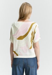 Pull en tricot blanc avec des motifs abstraits multicolores en rose et vert olive, doté de manches courtes et d'une coupe décontractée.