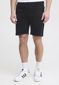 Shorts de algodón negro con ribs, con cintura ajustable de cordón y bolsillo con cremallera lateral, combinados con calcetines deportivos blancos y zapatillas blancas clásicas.