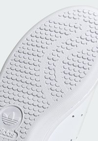 Λευκή σόλα αθλητικού παπουτσιού με υφασμάτινη κυκλική υφή και κυματιστό σχέδιο. Περιλαμβάνει ορατό λογότυπο και ομαλή τελείωση της άκρης.