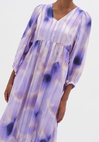 Purple and lilac patterned dress with a V-neck, long puffed sleeves, pleated bodice, and a flowing, textured skirt featuring dark spots.