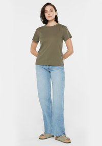 Olive green cotton t-shirt with short sleeves, round neckline, paired with light blue wide-leg jeans and flat sandals, featuring minimal design details.