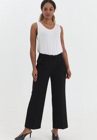Zwarte wijde pantalon met een elastische taille en trekkoord, gecombineerd met een witte mouwloze top. Gladde stof met een ontspannen pasvorm.