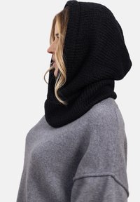 Czarny, dziany szal z kapturem o teksturowanym wykończeniu, zestawiony z szarym swetrem o luźnym kroju i subtelnymi akcentami w prążki.