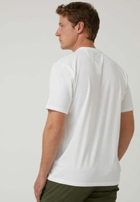 Camiseta blanca de manga corta hecha de algodón, con escote redondo, ajuste relajado y textura suave, mostrada desde la parte trasera.