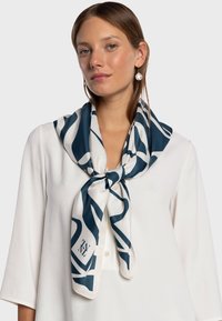 Écharpe en soie avec un motif abstrait bleu marine et blanc, nouée autour du cou. Le mannequin porte un chemisier blanc. Texture lisse, design élégant.
