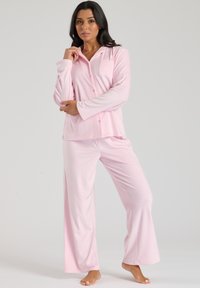 Lyserød pyjamas sæt lavet af blødt stof, med en langærmet skjorte med knapper og en lomme samt løstsiddende bukser med brede ben.