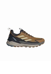 Buty do biegania po szlakach w brązowo-czarnym kolorze z teksturowaną cholewką, trzema białymi paskami, amortyzowaną podeszwą i ruggedową podszewką zapewniającą przyczepność.