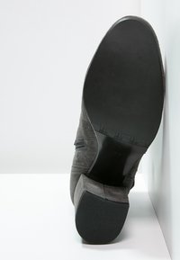 Graue Wildleder-Stiefelette, die auf der Seite liegt und die glatte schwarze Sohle sowie den Blockabsatz in Größe 37 zeigt, vor einem weißen Hintergrund.