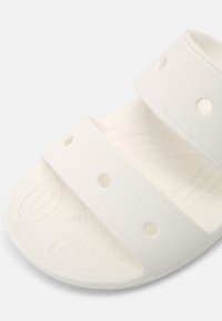 Gros plan d'une sandale en caoutchouc blanche avec deux larges brides présentant des trous de ventilation ronds et une semelle intérieure texturée pour l'adhérence.