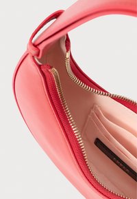 Koralowa skórzana torba o gładkim wykończeniu, ze złotym zamkiem błyskawicznym i czerwonym wnętrzem. Posiada jedną rączkę i widoczne wewnątrz przegródki na karty.