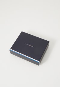Marineblaue Box mit einer glatten Textur, die ein weißes und rotes gestreiftes Akzentband aufweist. Das Logo "TOMMY HILFIGER" ist in weiß auf der Oberseite aufgedruckt.