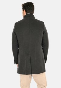 Cappotto in lana grigio scuro con collo alto, design sartoriale e un'unica spaccatura sul retro. Presenta maniche lunghe e spalle strutturate.