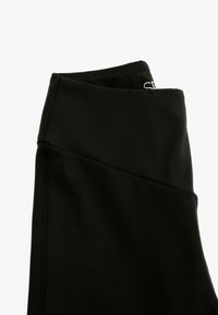 Zwarte legging van rekbaar materiaal, met een hoge tailleband, paneelontwerp en platte naden voor comfort. Geen patronen of hardware zichtbaar.