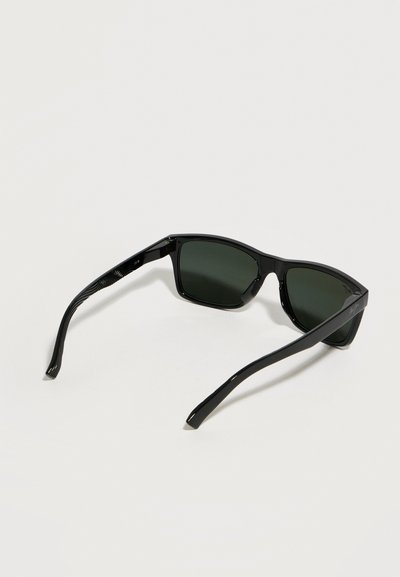 Μαύρα ορθογώνια γυαλιά ηλίου με σκουρόχρωμους φακούς και ελαφρώς καμπύλα μπράτσα, εμφανιζόμενα σε λευκό απλό φόντο.