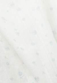 Tejido blanco ligero que presenta un sutil patrón floral azul, texturizado con pequeños diamantes en relieve y delicados detalles de costura.