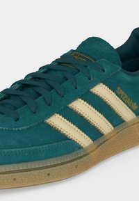 Baskets en daim bleu sarcelle avec des bandes Adidas crème, semelle en gomme, lacets, et marquage "Spezial" doré sur le côté.